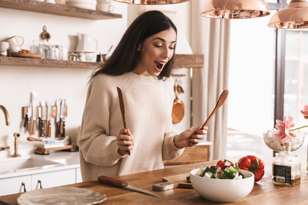 Picture of attractive brunette woman 30s cooking healthy green salad with vegetables in stylish kitchen at homeの写真素材