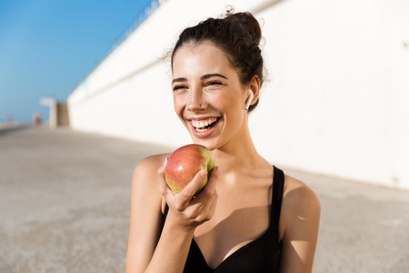 Attractive smiling sportswoman resting after workout outdoors, showing appleの写真素材