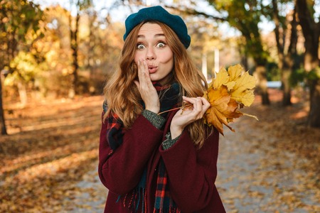 Cheerful young girl with long brown hair wearing autumn coat, walking at the parkの写真素材