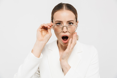 Photo of shocked businesswoman 20s wearing elegant jacket looking at camera and holding eyeglasses isolated over white backgroundの写真素材