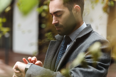 Cheerful young businessman wearing suit walking outdoors, checking timeの写真素材
