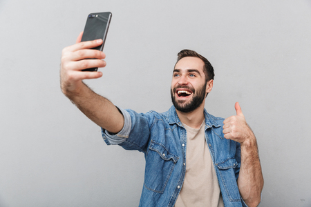 Excited cheerful man wearing shirt isolated over gray background, taking a selfieの写真素材