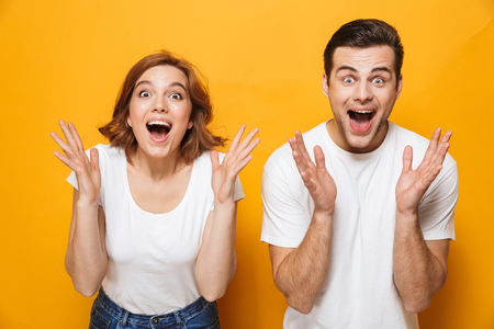 Portrait of a cheerful young couple standing isolated over yellow background, celebrating successの写真素材