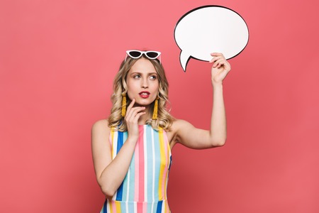 Image of a beautiful thinking young woman posing isolated over red coral background holding speech bubble.の写真素材