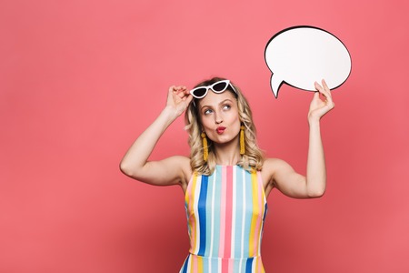 Image of a beautiful thinking young woman posing isolated over red coral background holding speech...