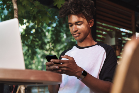 Young african teenager student sitting at the cafe indoors, using mobile phoneの写真素材