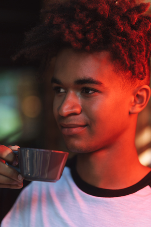 Smiling african young man drinking coffee at the cafe indoors