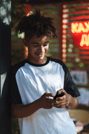 Smiling african young man using mobile phone at the cafe indoorsの写真素材