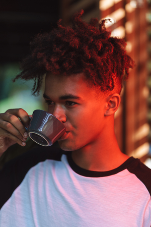 Smiling african young man drinking coffee at the cafe indoorsの写真素材