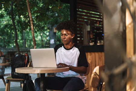 Young african man using laptop computer at the cafe outdoors, drinking coffeeの写真素材