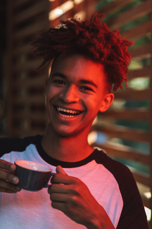 Smiling african young man drinking coffee at the cafe indoorsの写真素材