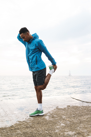 Photo of a strong handsome young african sports man outdoors at the beach sea walking make...