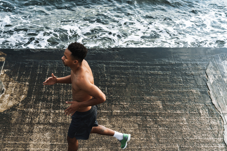Photo of a strong handsome young african sports man runner outdoors at the beach sea running make exercises.の写真素材