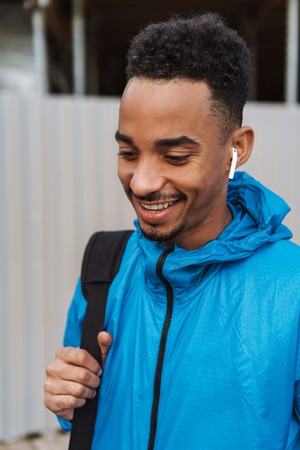 Picture of a handsome happy young african sports man outdoors at the beach sea walking with bag listening music with earphones.の写真素材