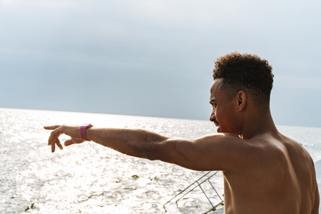 Image of a handsome young african sports man outdoors at the beach sea pointing.の写真素材