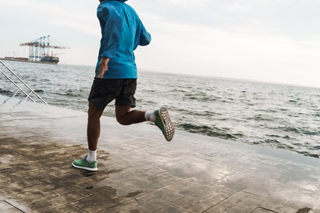Cropped photo of a strong handsome young african sports man runner outdoors at the beach sea running make exercises.の写真素材
