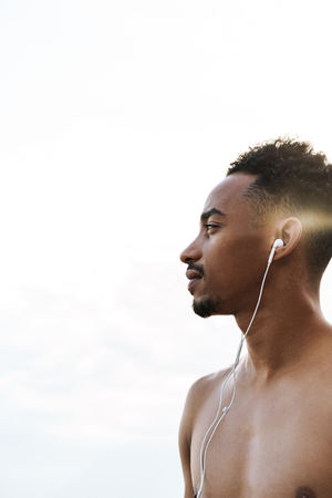 Photo of a strong handsome young african sports man outdoors at the beach sea listening music with earphones.の写真素材