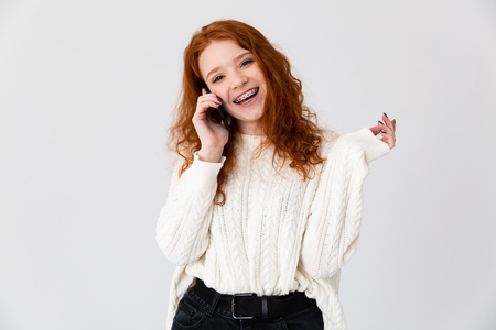 Image of a beautiful young girl redhead posing isolated over white wall background talking by phone.の写真素材