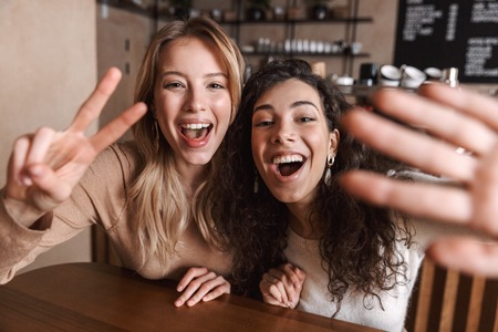 Image of excited happy pretty girls friends sitting in cafe take a selfie by camera.の写真素材