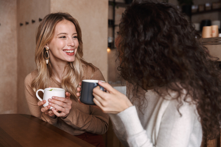 Image of a happy girls friends sitting in cafe talking with each other drinking tea or coffee.の写真素材