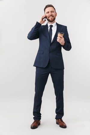 Image of young happy businessman posing isolated over white wall background drinking coffee talking by phone.の写真素材