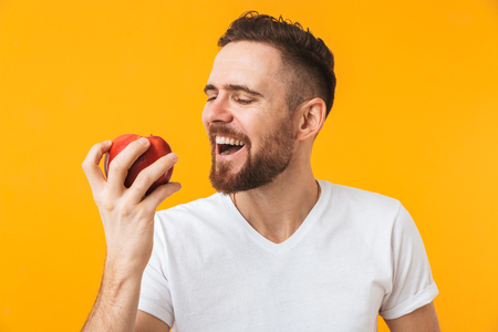 Photo of a happy young handsome man posing isolated over yellow wall background holding apple.の写真素材