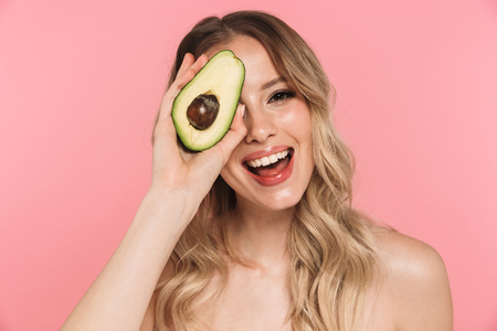 Beauty portrait of a lovely young woman with long blonde hair standing isolated over pink background, showing avocadoの写真素材