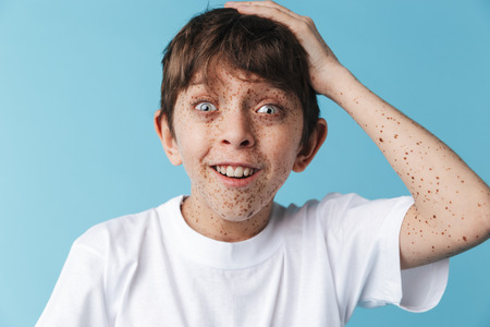 Image closeup of cheery caucasian boy 10-12y with freckles wearing white casual t-shirt smiling at...