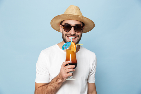 Cheerful excited man wearing blank t-shirt standing isolated over blue background, drinking cocktail, having funの写真素材