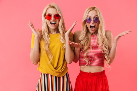 Happy blonde twins in sunglasses rejoices and looking at the camera over pink backgroundの写真素材