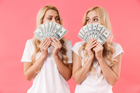 Mystery blonde twins wearing in t-shirts covering her faces and looking to each other over pink backgroundの写真素材