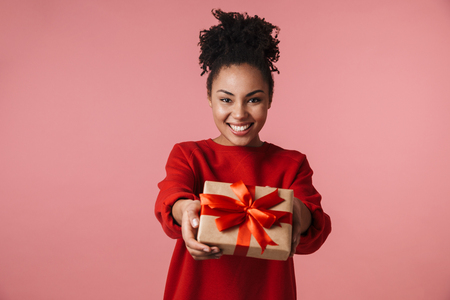Image of a beautiful amazing happy excited young african woman posing isolated over pink wall background holding present box.の写真素材