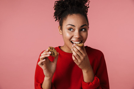 Image of a beautiful amazing happy excited young african woman posing isolated over pink wall background holding sweeties cookies.の写真素材