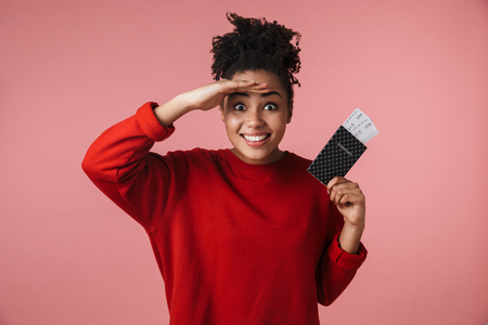 Image of a beautiful amazing happy excited young african woman posing isolated over pink wall background holding passport with tickets.の写真素材