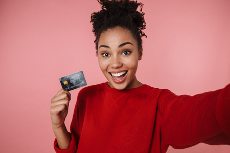 Image of a beautiful amazing happy excited young african woman posing isolated over pink wall background take selfie by camera with credit card.の写真素材