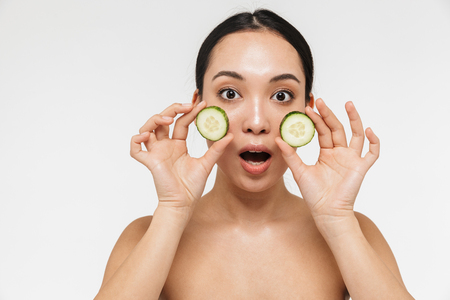 Photo of a beautiful young pretty asian woman with healthy skin posing naked isolated over white wall background holding cucumber.の写真素材