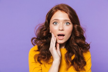Portrait of a pretty excited young redheaded woman standing isolated over violet backgroundの写真素材