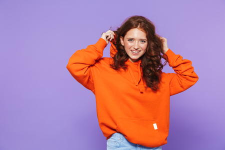 Portrait of a pretty young redheaded woman standing isolated over violet background, posing, gesturingの写真素材