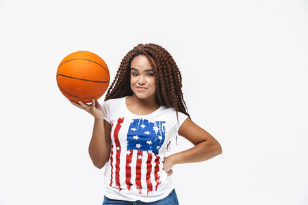 Portrait of brunette african american woman rejoicing and holding basketball during game while standing isolated against white wallの写真素材