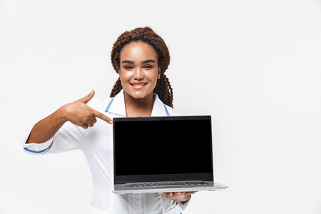 Image of joyous african american nurse or doctor woman wearing medical coat holding laptop isolated against white backgroundの写真素材