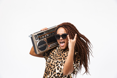 Image of delighted african american woman smiling and holding vintage boombox with cassette tape on her shoulder isolated against white backgroundの写真素材