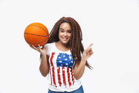 Portrait of energetic african american woman rejoicing and holding basketball during game while standing isolated against white wallの写真素材