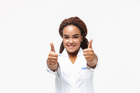 Image of happy african american nurse or doctor woman smiling and showing thumbs up isolated against white backgroundの写真素材