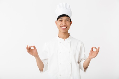 Excited asian chef wearing uniform standing isolated over white background, gesturing, okの写真素材