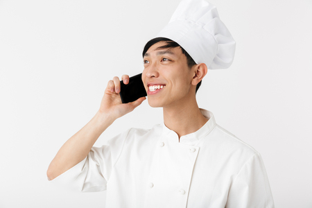 Excited asian chef wearing uniform standing isolated over white backgroundの写真素材