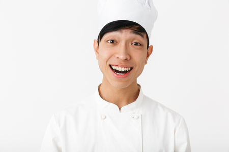 Image of asian happy chief man in white cook uniform smiling at camera while standing isolated over white backgroundの写真素材