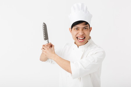 Image of asian joyful chief man in white cook uniform smiling at camera while holding big knife isolated over white backgroundの写真素材