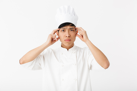 Confused asian chef wearing uniform standing isolated over white backgroundの写真素材