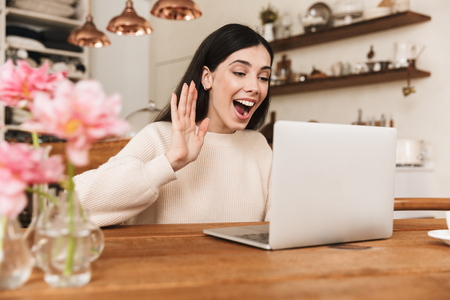 Smiling young woman sitting at the kitchen and using laptop computer, having video callの写真素材