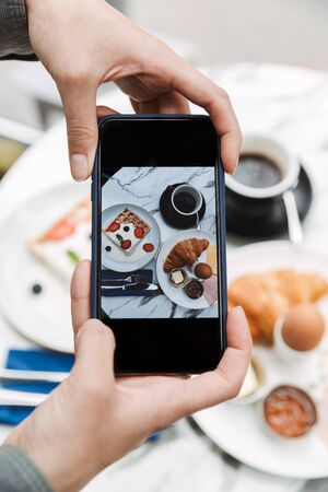 Close up of a woman taking photo of breakfast served in cafeの写真素材